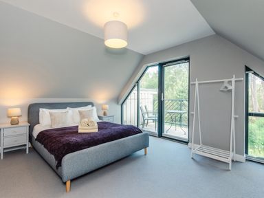 A bedroom with a bed and bedside tables with lamps and a clothing rack next to glass doors opening to a balcony at Otter Lodge in Feshiebridge near Aviemore
