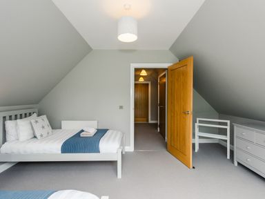 A bedroom with a bed with pillows and a blue blanket a dresser an open wooden door and a clothes rack at Otter Lodge in Feshiebridge near Aviemore