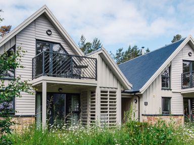 The exterior of a two-story house with balconies and wildflowers in front at Otter Lodge in Feshiebridge near Aviemore