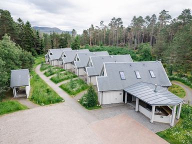 A row of six houses with grey roofs surrounded by trees and greenery at Otter Lodge in Feshiebridge near Aviemore