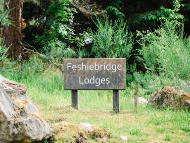 A sign reading Feshiebridge Lodges surrounded by grass rocks and trees