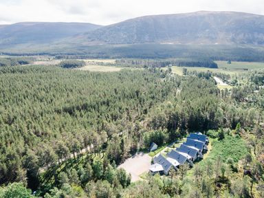 An aerial view of a forest with a row of buildings and mountains in the background at Otter Lodge in Feshiebridge near Aviemore