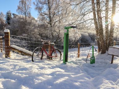 A bicycle with a basket near a pump in snow at Otter Lodge in Feshiebridge near Aviemore