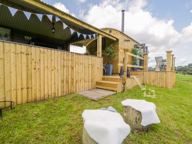 A wooden cabin with a deck and outdoor seating on a grassy lawn with croquet set at High Rigg Shepherd's Retreat in Brampton Cumbria