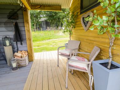 An outdoor seating area with two chairs on a wooden deck beside a wooden wall with potted plants and a lantern at High Rigg Shepherd's Retreat in Brampton Cumbria
