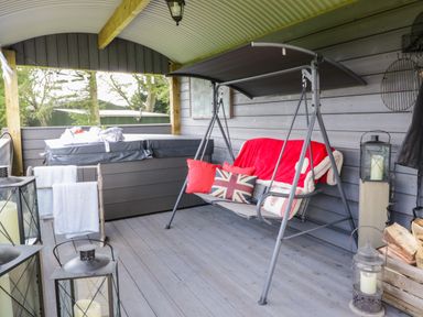 A covered outdoor seating area with a swing bench with cushions and a hot tub at High Rigg Shepherd's Retreat in Brampton Cumbria