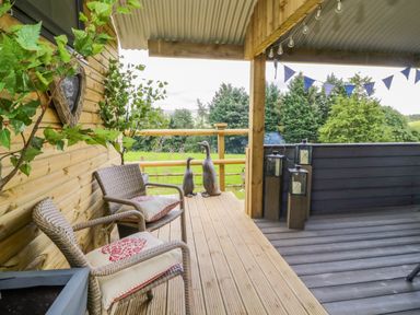 A wooden deck with two chairs and cushions metal duck statues and lanterns at High Rigg Shepherd's Retreat in Brampton Cumbria