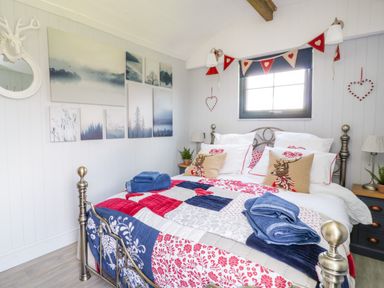 A bedroom with a metal bed frame blue red and white bedding and artwork on the wall at High Rigg Shepherds Retreat in Brampton Cumbria