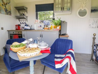 A small kitchen with gray cabinets and a wooden countertop with blue chairs and a round table with food on it at High Rigg Shepherd's Retreat in Brampton Cumbria