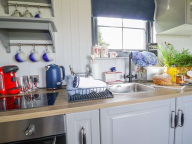 A kitchen counter with a sink a red coffee machine blue kettle mugs flowers bread and orange juice at High Rigg Shepherd's Retreat in Brampton Cumbria