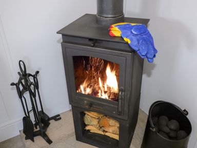 A wood burning stove with fire inside gloves on top fire tools on the left and a black container with coal on the right at High Rigg Shepherd's Retreat in Brampton Cumbria