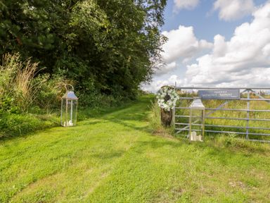 A grassy path between trees and a gate with lanterns and a daisy wreath at High Rigg Shepherd's Retreat in Brampton Cumbria