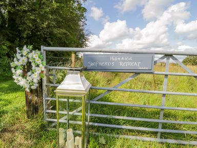 A metal gate with a sign reading High Rigg Shepherds Retreat and a wreath of white flowers on a post next to a lantern with candles at High Rigg Shepherd's Retreat in Brampton Cumbria