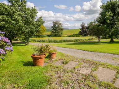 A gravel pathway with potted plants beside a green lawn and trees at High Rigg Shepherd's Retreat in Brampton Cumbria
