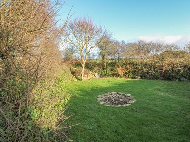 A garden with grass a stone fire pit and leafless trees at Kernyk in Rinsey near Porthleven