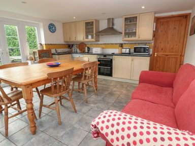 A kitchen with wooden table and chairs a red sofa and wooden cabinets at Kernyk in Rinsey near Porthleven