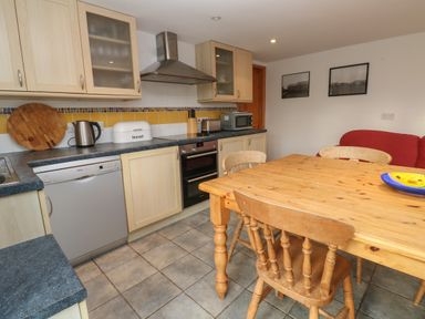 A kitchen with wooden cabinets a dining table with chairs and a red sofa at Kernyk Rinsey near Porthleven