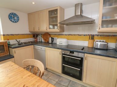 A kitchen with wooden cabinets a dishwasher an oven a stovetop and a wooden dining table at Kernyk in Rinsey near Porthleven