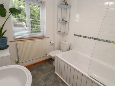 A bathroom with a bathtub a toilet a window with blinds a radiator a plant and a corner shelf at Kernyk Rinsey near Porthleven