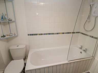 A bathroom with a bathtub and shower unit next to a toilet and shelving at Kernyk in Rinsey near Porthleven