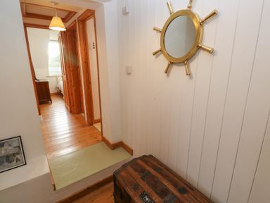A hallway with wooden floors a round mirror on the wall and a wooden chest at Kernyk Rinsey near Porthleven