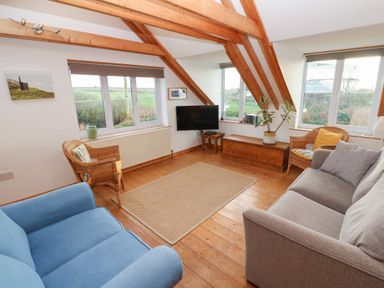 A living room with wooden beams a blue armchair two wicker chairs a gray sofa and a wall-mounted TV at Kernyk in Rinsey near Porthleven