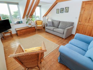 A living room with a grey sofa blue armchair wicker chairs wooden chest a television and framed pictures at Kernyk Rinsey near Porthleven