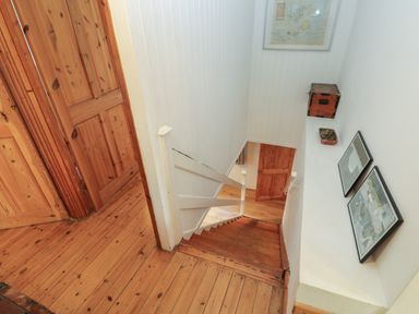 A wooden staircase leading down with wooden doors and framed pictures on white walls at Kernyk in Rinsey near Porthleven