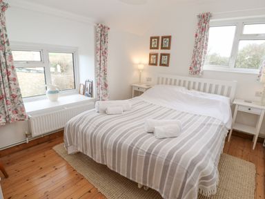 A bedroom with a double bed and striped bedding with floral curtains at Kernyk in Rinsey near Porthleven