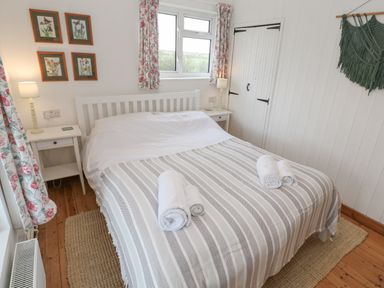 A bedroom with a double bed and rolled towels on a striped blanket two bedside tables with lamps framed pictures on the wall and floral curtains at Kernyk Rinsey near Porthleven