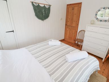 A bedroom with a bed towels wooden chair white dresser and wooden door at Kernyk Rinsey near Porthleven