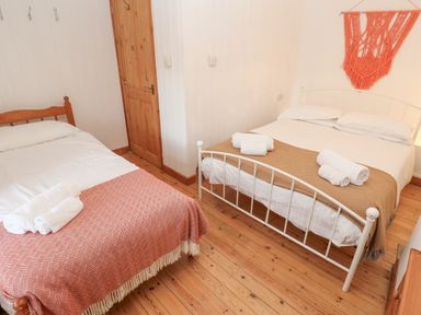 A bedroom with two beds, towels on each bed, wooden door and floor, and a wall hanging at Kernyk in Rinsey near Porthleven