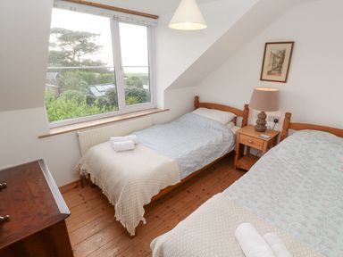 A bedroom with two single beds a wooden nightstand with a lamp a wooden dresser and a large window overlooking greenery at Kernyk in Rinsey near Porthleven