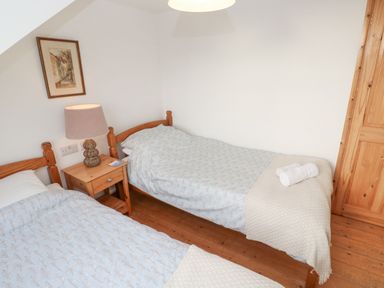 A bedroom with two single beds a wooden nightstand with a lamp a framed picture on the wall at Kernyk Rinsey near Porthleven