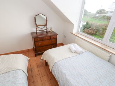 A bedroom with two single beds a wooden dresser with a mirror and a window showing greenery at Kernyk in Rinsey near Porthleven
