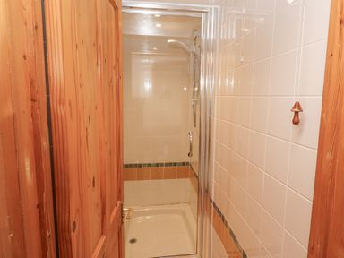 A shower cubicle with a glass door in a bathroom with tiled walls and a wooden door at Kernyk in Rinsey near Porthleven