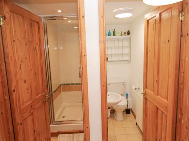 A bathroom with a shower stall and a toilet with sink separated by wooden doors at Kernyk Rinsey near Porthleven
