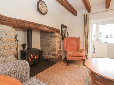 A living room with a fireplace and an armchair at Kernyk in Rinsey near Porthleven