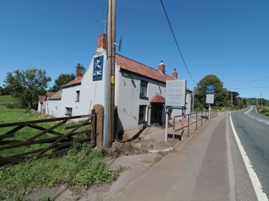 A traditional country pub near a road with signs advertising food and drinks at The Cider Shed in Winscombe
