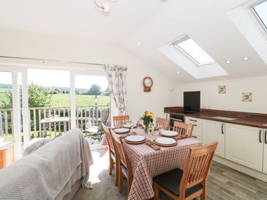 A dining area with a table set for six and a kitchen with white cabinets and skylights at The Cider Shed in Winscombe