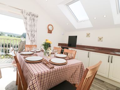 A dining area with a wooden table set for six with plates and glasses and a kitchen in the background at The Cider Shed in Winscombe