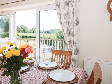 A dining table set with plates glasses and napkins next to a sliding door opening to a balcony with outdoor furniture at The Cider Shed in Winscombe