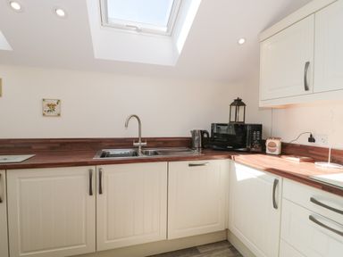 A kitchen with white cabinets wooden countertops a sink microwave and kettle under a skylight at The Cider Shed in Winscombe