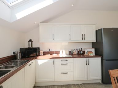 A kitchen with white cabinets wooden countertops a black microwave kettle and stainless steel sink at The Cider Shed in Winscombe