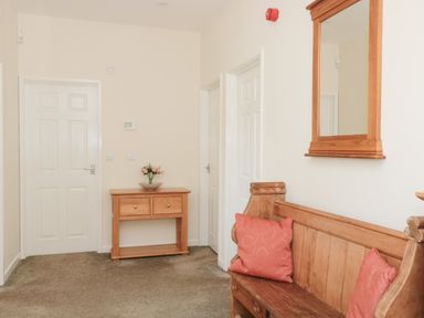 A hallway with a wooden bench with cushions a wooden console table with flowers and doors at The Cider Shed in Winscombe