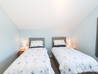 A bedroom with two single beds with floral bedding and bedside tables with lamps at The Cider Shed in Winscombe