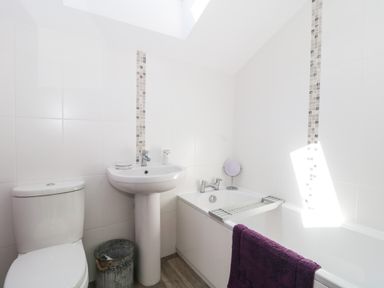 A bathroom with a toilet a pedestal sink a bathtub with a purple towel and a small mirror at The Cider Shed in Winscombe