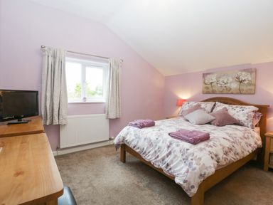 A bedroom with a double bed with floral bedding a television on a wooden dresser and a window with curtains at The Cider Shed in Winscombe