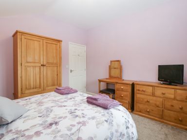A bedroom with a wooden wardrobe a dressing table a chest of drawers and a bed with floral bedding at The Cider Shed in Winscombe