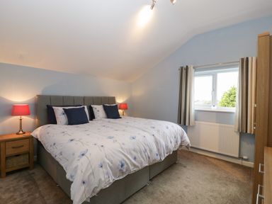 A bedroom with a double bed with floral bedding two bedside tables with lamps a window with curtains and a wardrobe at The Cider Shed in Winscombe